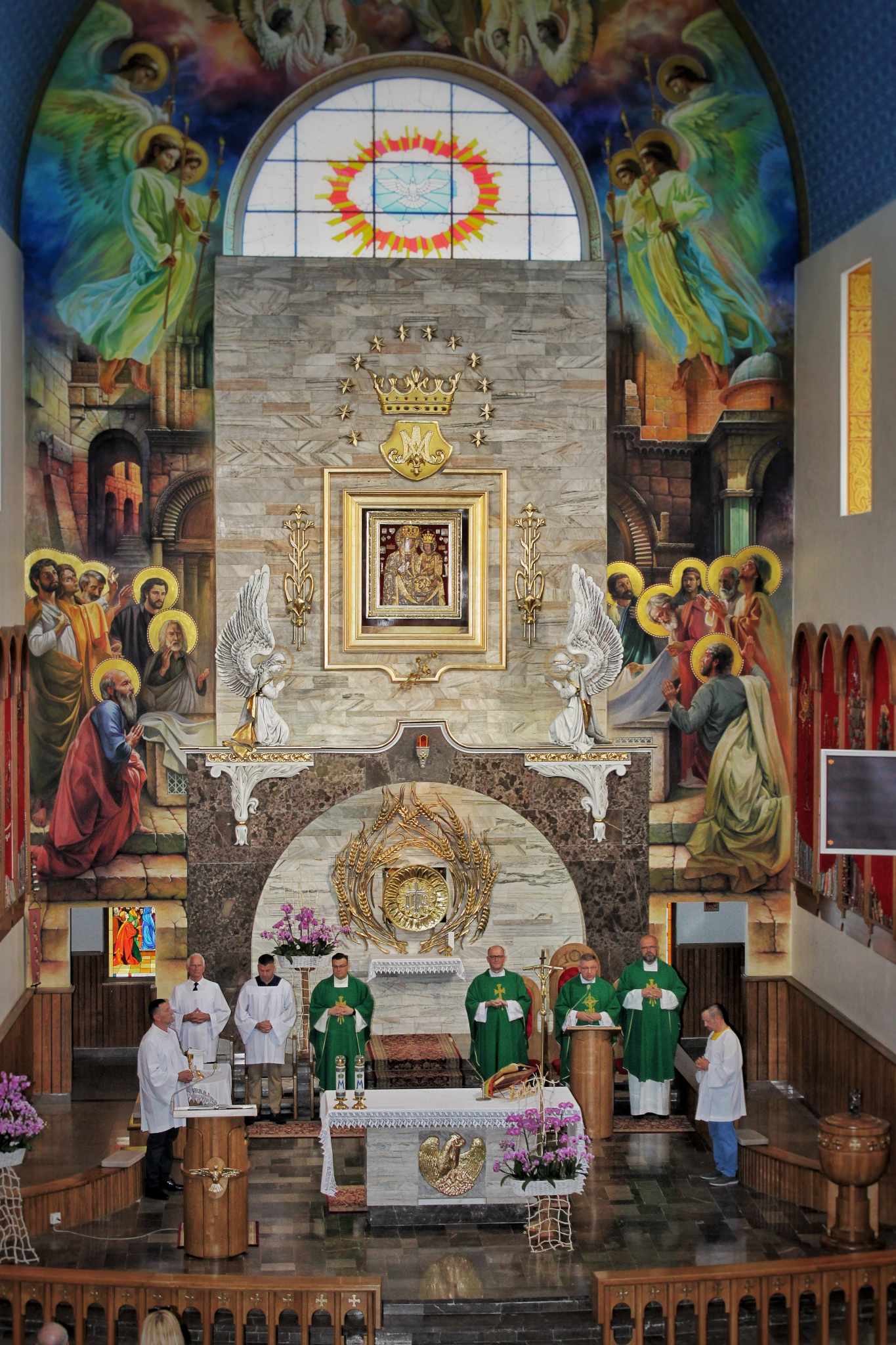 Kościelny ołtarz z ambo i ołtarzem eucharystycznym. W tle malowidło na ścianie. Kilku mężczyzn w szatach kościelnych stoi wokół ołtarza.
