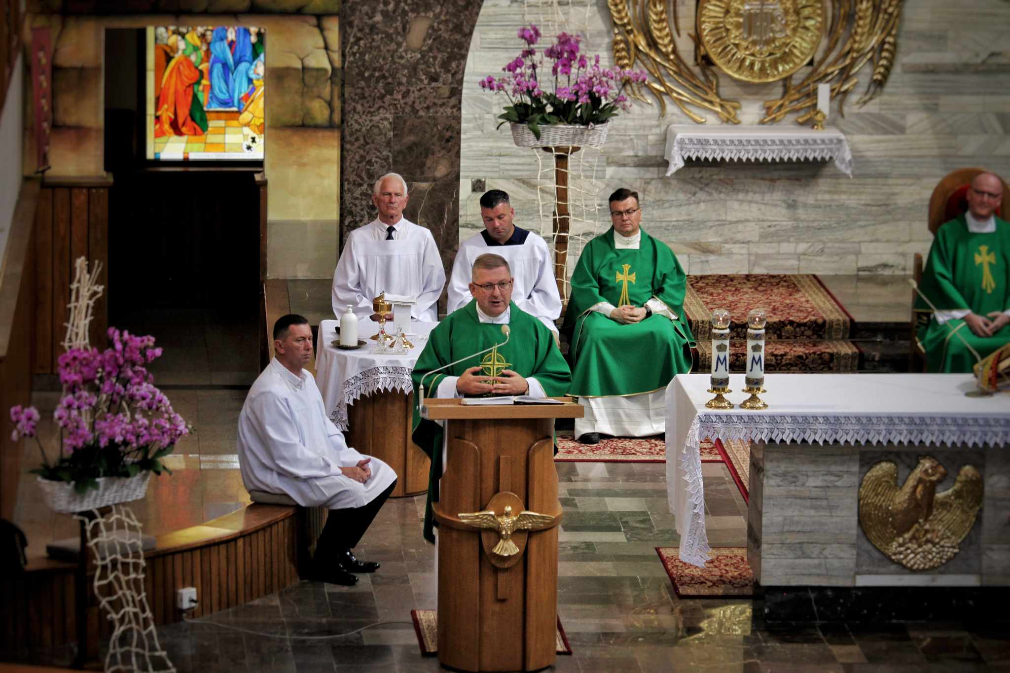 Kapłan przemawia przy ambonie podczas Eucharystii; za nim przy ołtarzu siedzą pozostali duchowni i ministranci.