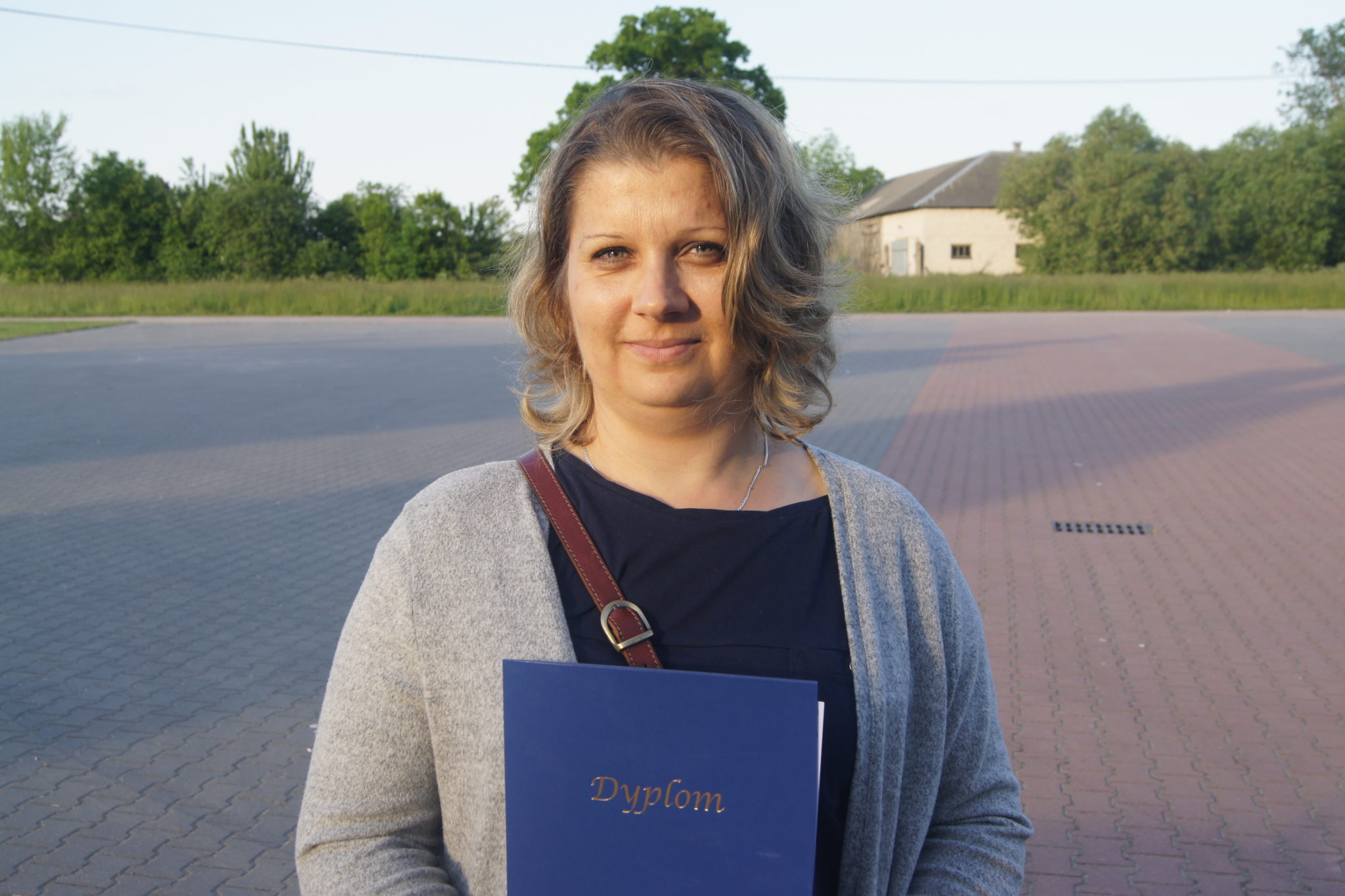 Kobieta trzyma dyplom na tle placu i budynku.